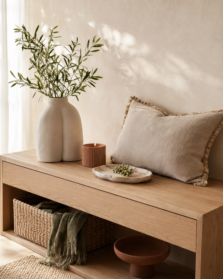 Ceramic vase, candle, linen cushions and woven basket on an oak console